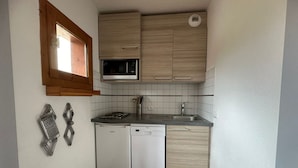 Una cocina compacta con microondas integrado, lavavajillas y fregadero.