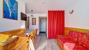 A room with a wooden dining table, chairs, a red sofa, a television, and a painting on the wall. - Spacious and bright apartment at the foot of the slopes with balcony (Les Menuires)