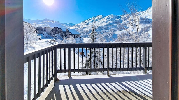 A balcony with a view of snow-covered mountains and a building in the background. - Spacious and bright apartment at the foot of the slopes with balcony (Les Menuires)