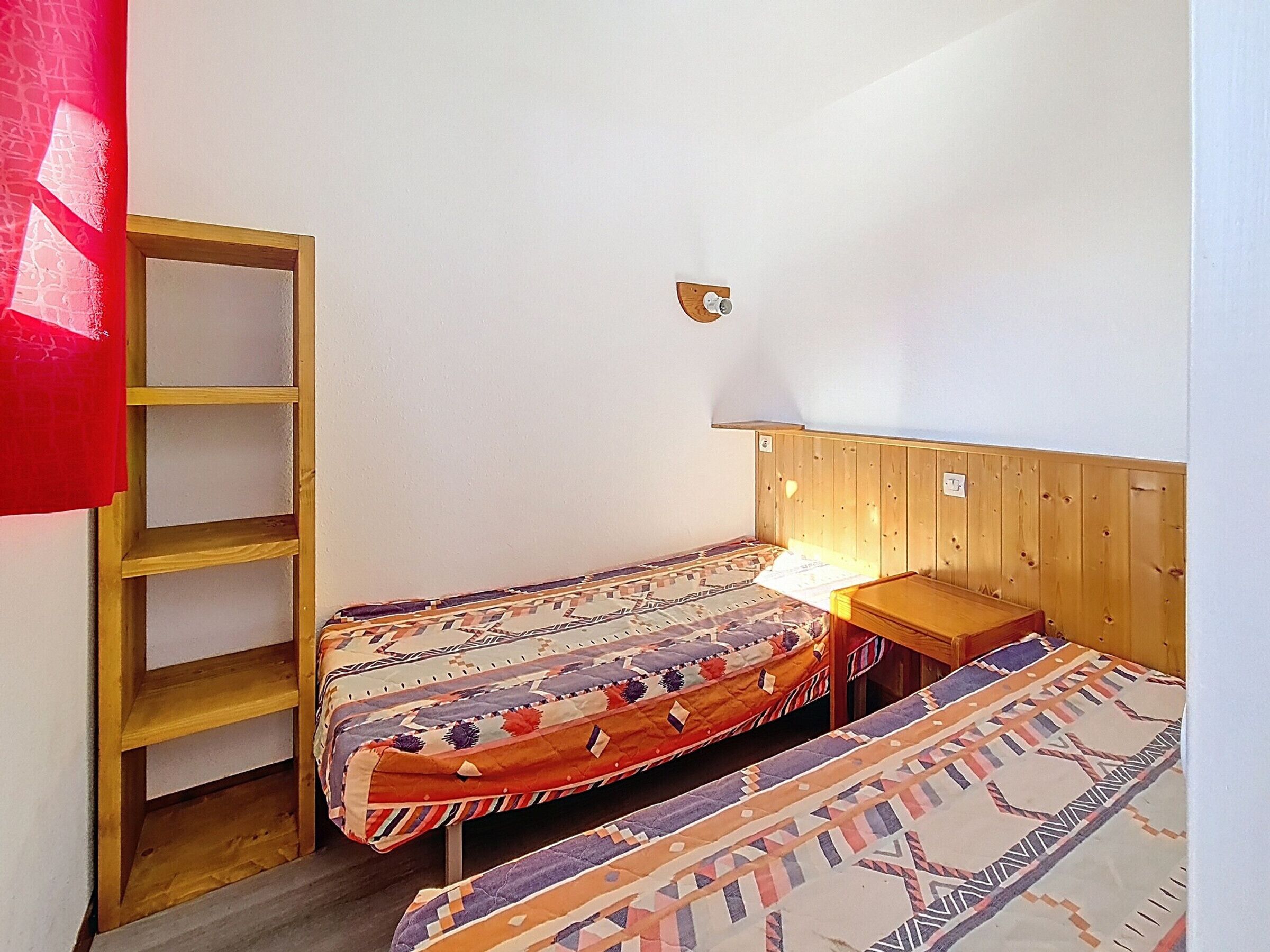 Una habitación pequeña y acogedora con dos camas individuales, cabecero de madera, una mesita y una lámpara fijada a la pared.