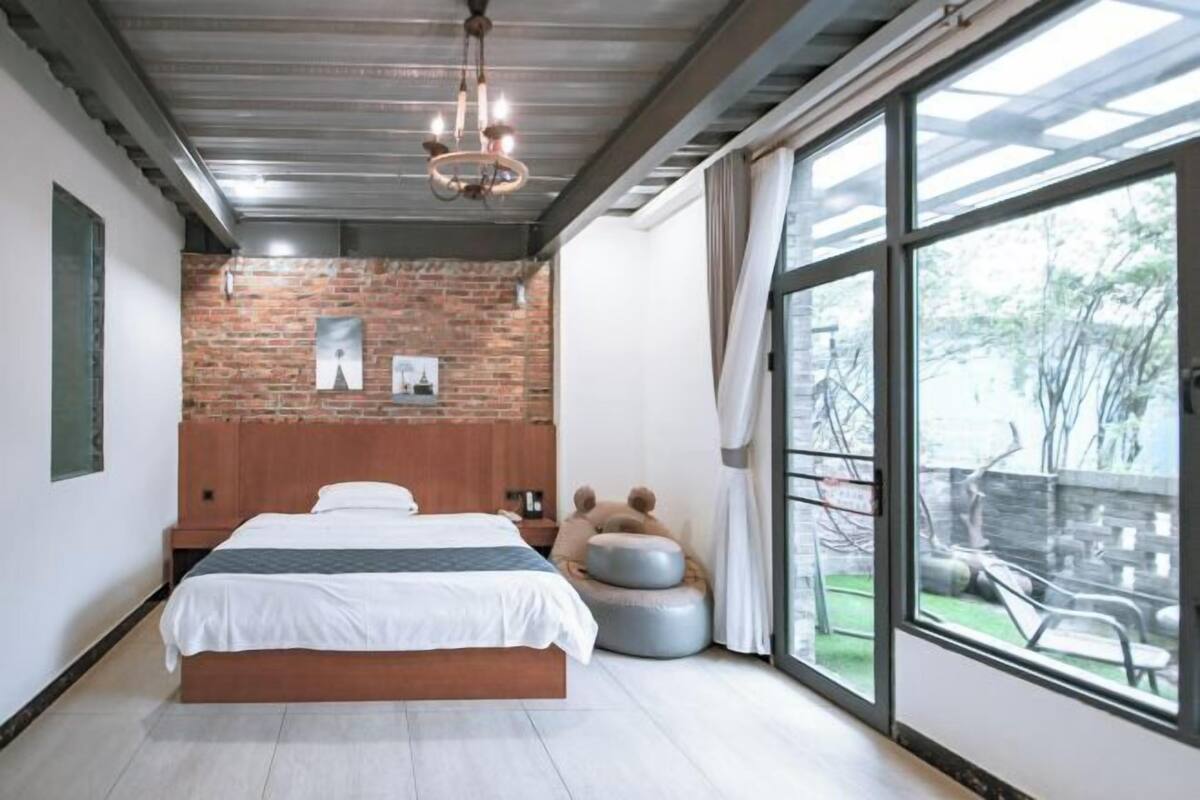 A bedroom with a large bed, a brick wall, a chandelier, and a view of the outdoors.