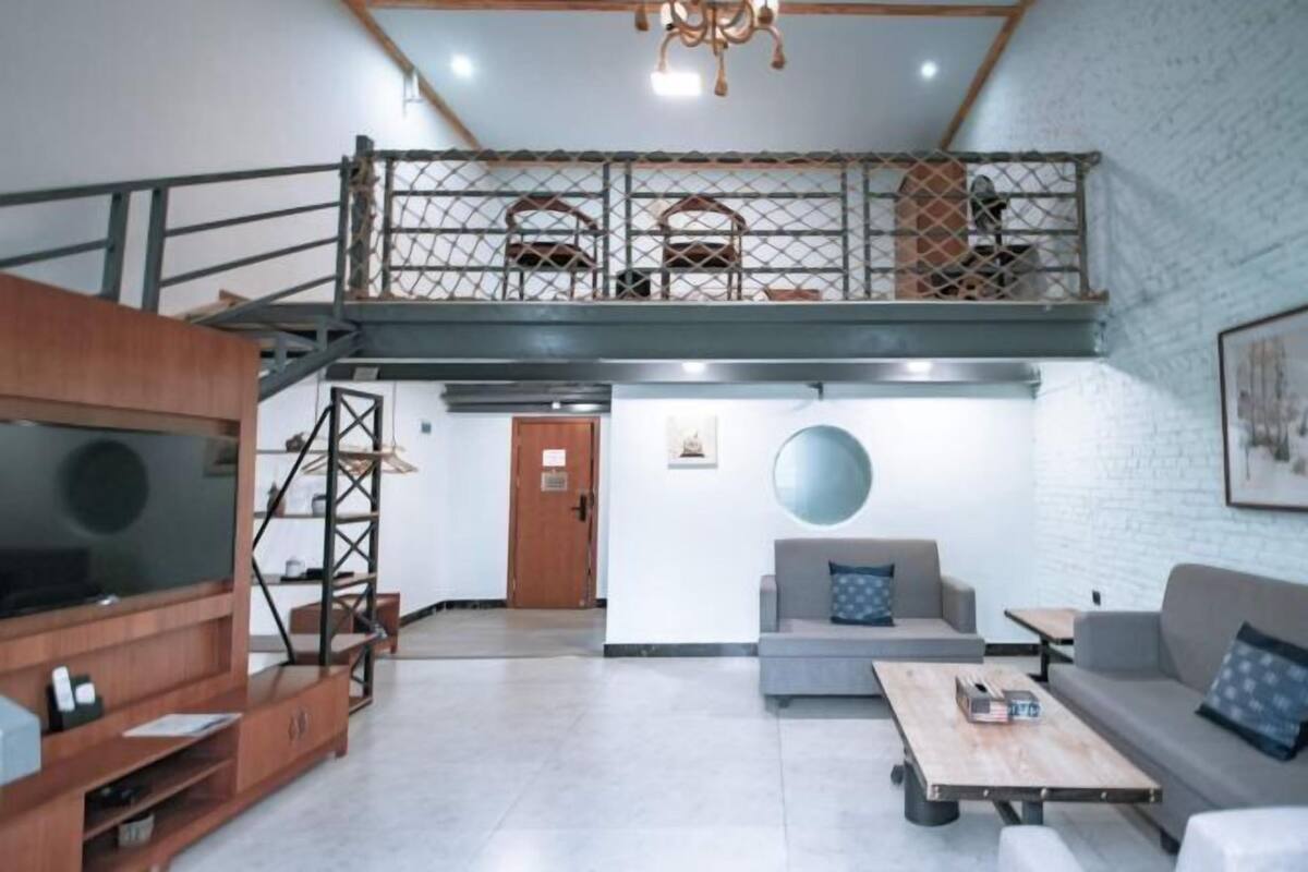 A spacious living area with a high ceiling, a staircase leading to an upper level, and a large flat-screen TV.