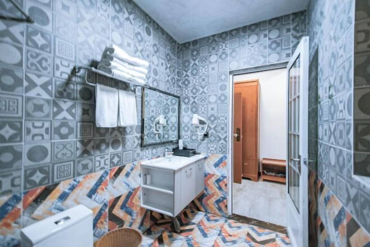 A bathroom with patterned tiles, a white sink, a mirror, and a towel rack.