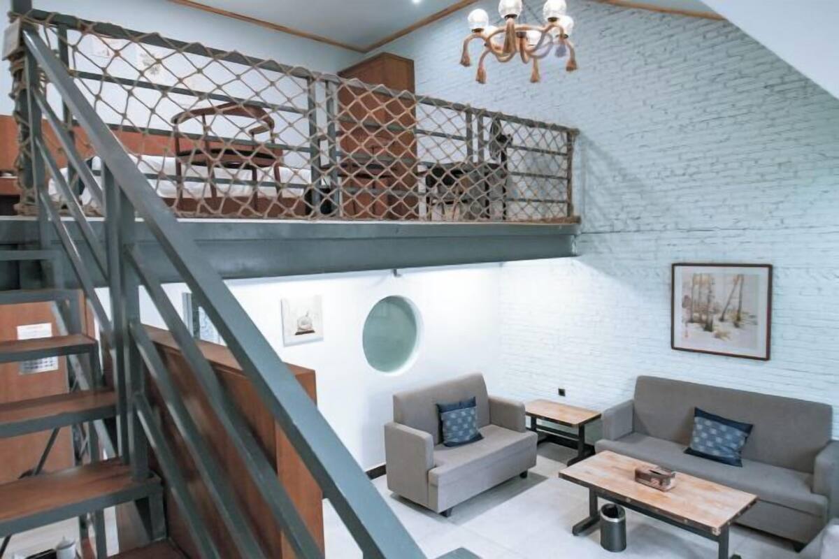 A loft-style room with a staircase, a mezzanine, a sofa, a coffee table, and a chandelier.