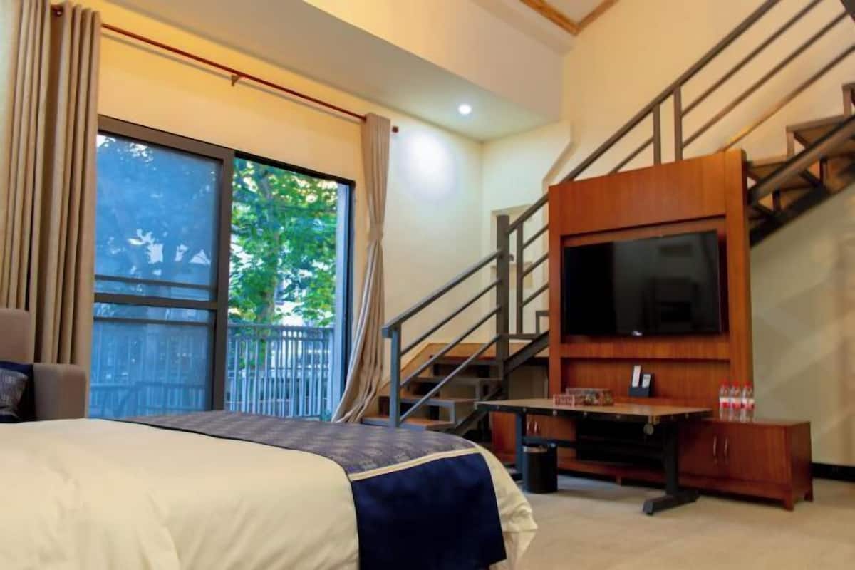 A hotel room with a bed, a TV, a desk with a chair, and a staircase.