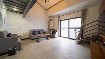 A spacious living room with a high ceiling, a staircase, and a large window.