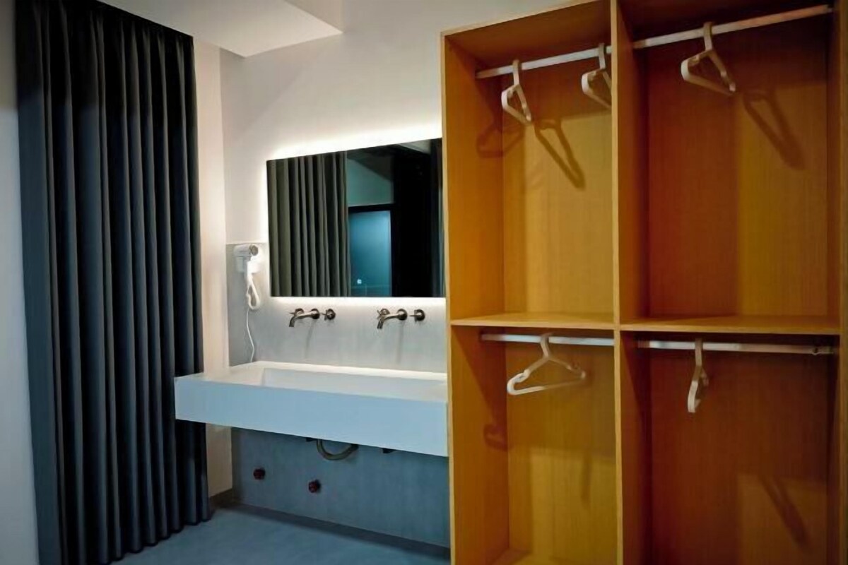 Un baño moderno con un lavamanos blanco, un espejo y un armario de madera con perchas.