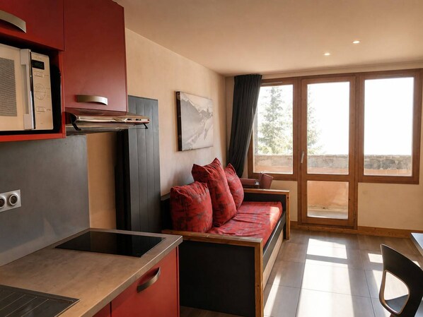 A modern kitchen with a built-in stove, a red sofa with cushions, and a dining area with a chair.
