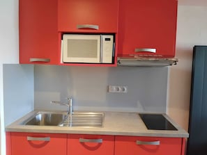 Cocina compacta con microondas integrado, un lavabo y armarios rojos.
