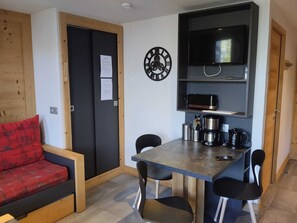 A compact living space with a kitchenette, a dining area with a table and chairs, a red sofa, and a clock on the wall.