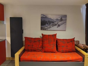 Una habitación con sofá cama, un cuadro de un paisaje montañoso nevado y un armario rojo.
