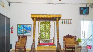 Une pièce spacieuse dotée d’un plancher en bois, de deux fauteuils décoratifs, d’un banc central avec un coussin rouge et d’un panneau mural décoratif.