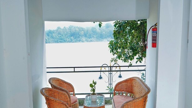Un balcon doté de meubles en osier et d’une petite table, offrant une vue sur une étendue d’eau et sur la verdure.