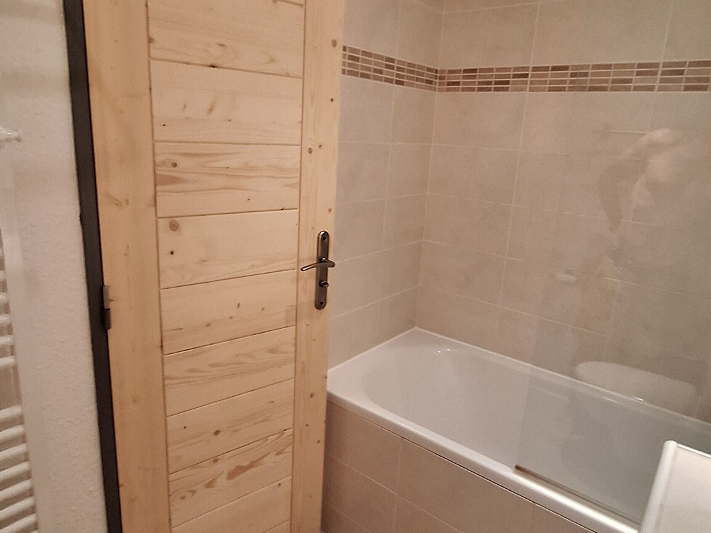 A wooden door with a handle, a white bathtub, and a tiled shower area.
