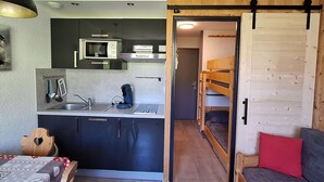 Eine kompakte Küche mit modernen Geräten, ein Essbereich mit Tisch und Stühlen sowie ein Schlafbereich mit Etagenbett.