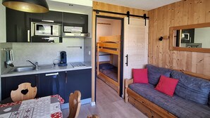 Ein kompakter Wohnbereich mit Küchenzeile, einer Couch und einem Etagenbett.
