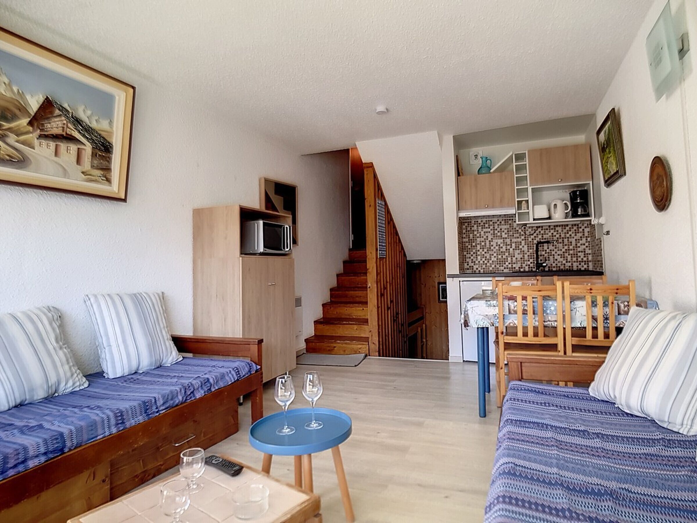 A cozy living room with a sofa, a small table with glasses, and a staircase leading to a kitchen.
