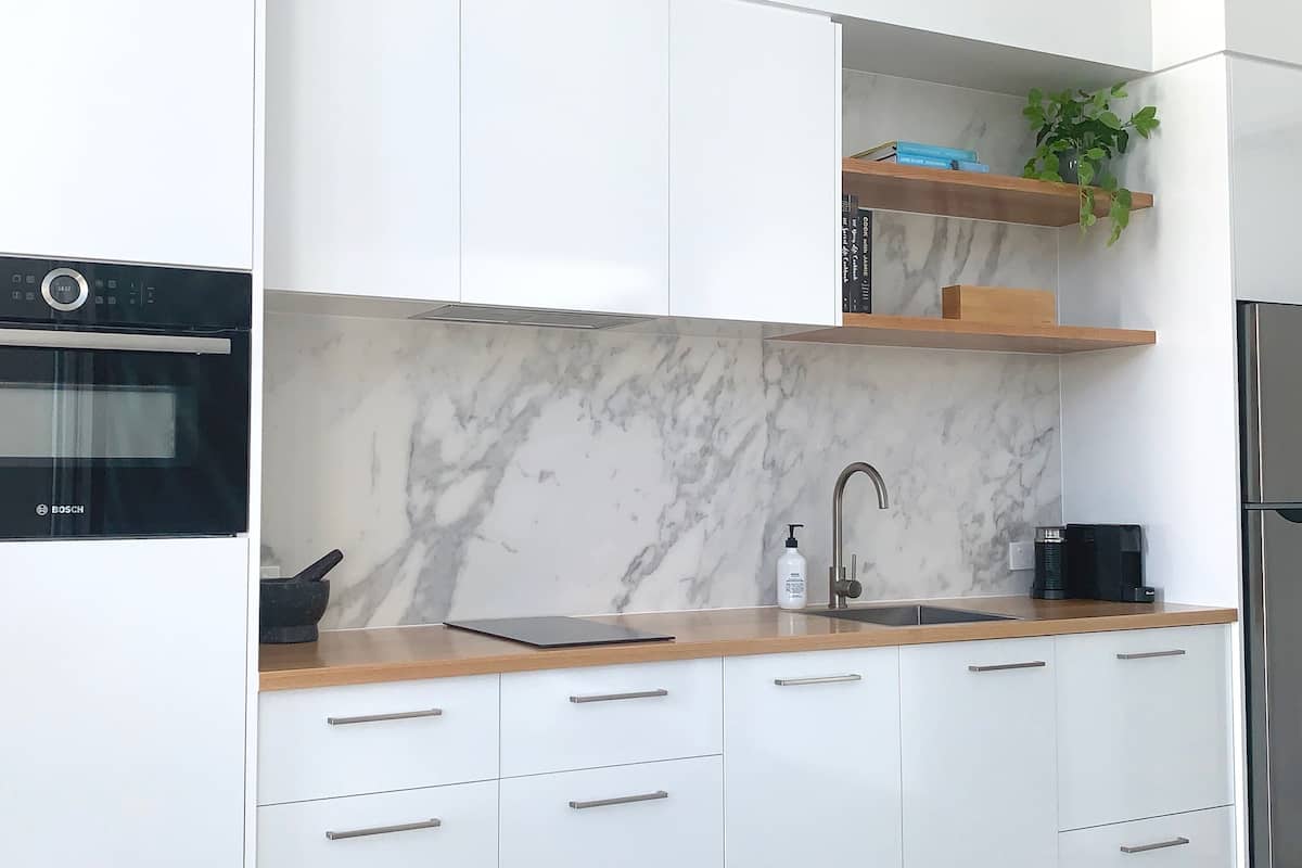 A modern kitchen with white cabinets, a marble backsplash, a Bosch oven, a stainless steel refrigerator, and a wooden countertop.