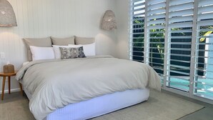 Quarto com cama, mesa de cabeceira e janela com persianas.