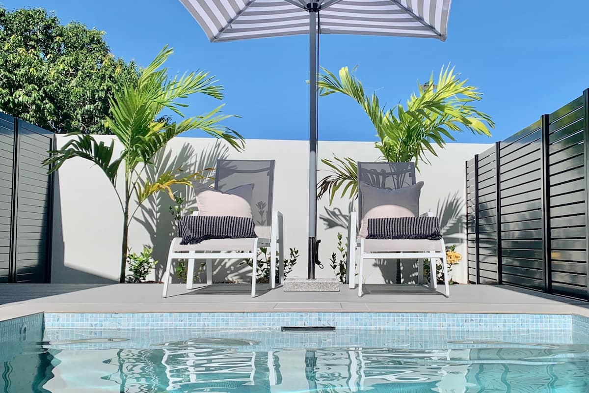 A swimming pool with two lounge chairs and an umbrella.