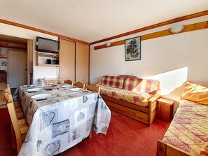 Una habitación compacta con una mesa de comedor dispuesta para cuatro personas, un sofá, una cama y un mueble pequeño.