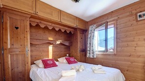 Une chambre dans une cabane en bois, avec deux lits, une fenêtre avec des rideaux et des armoires en bois.