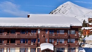 Een meerlaags hotel met een met sneeuw bedekte sneeuwkap, houten balkons en een berg op de achtergrond.