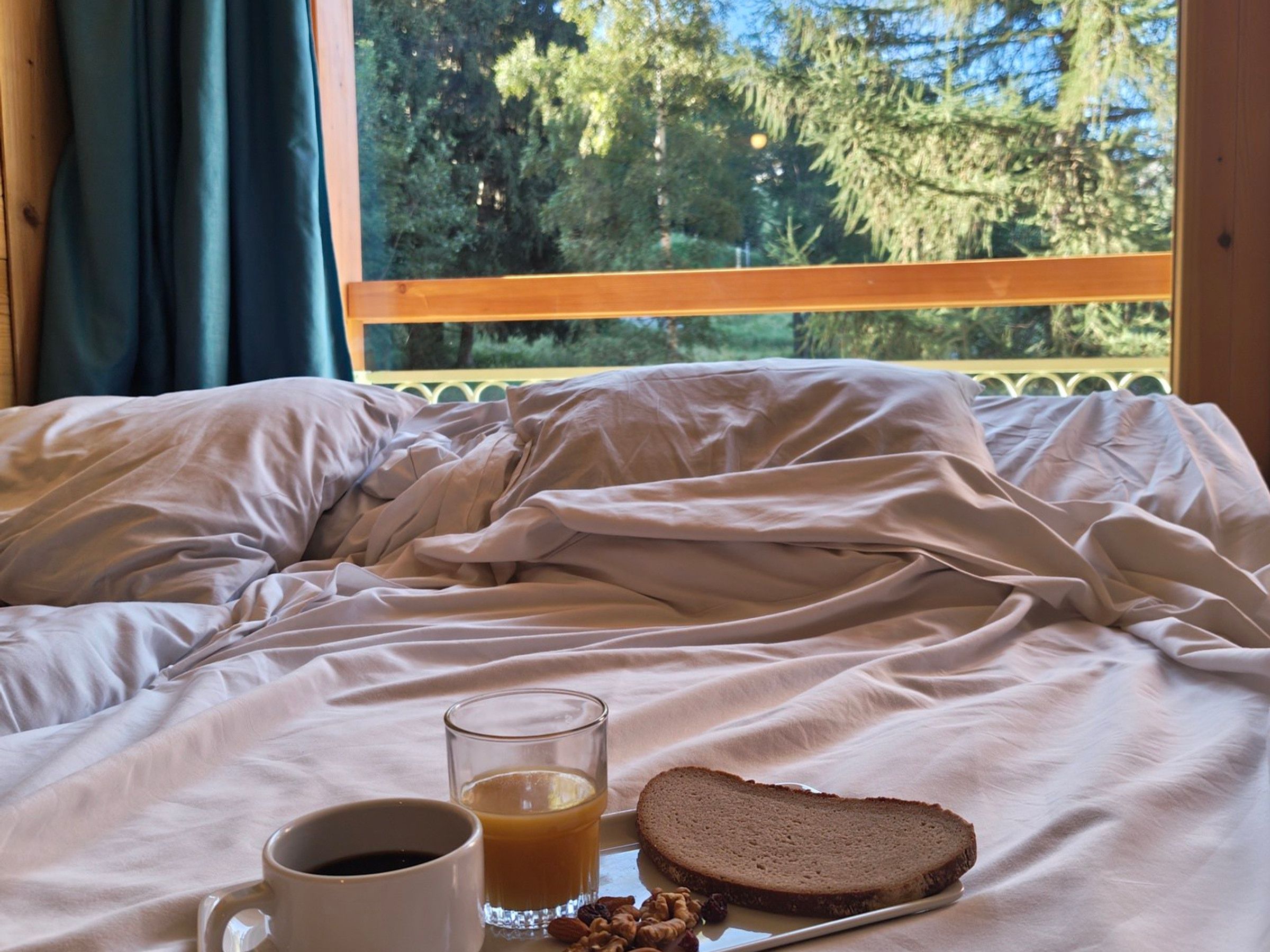 A bed with a glass of orange juice, a cup of coffee, and a slice of bread on a tray.