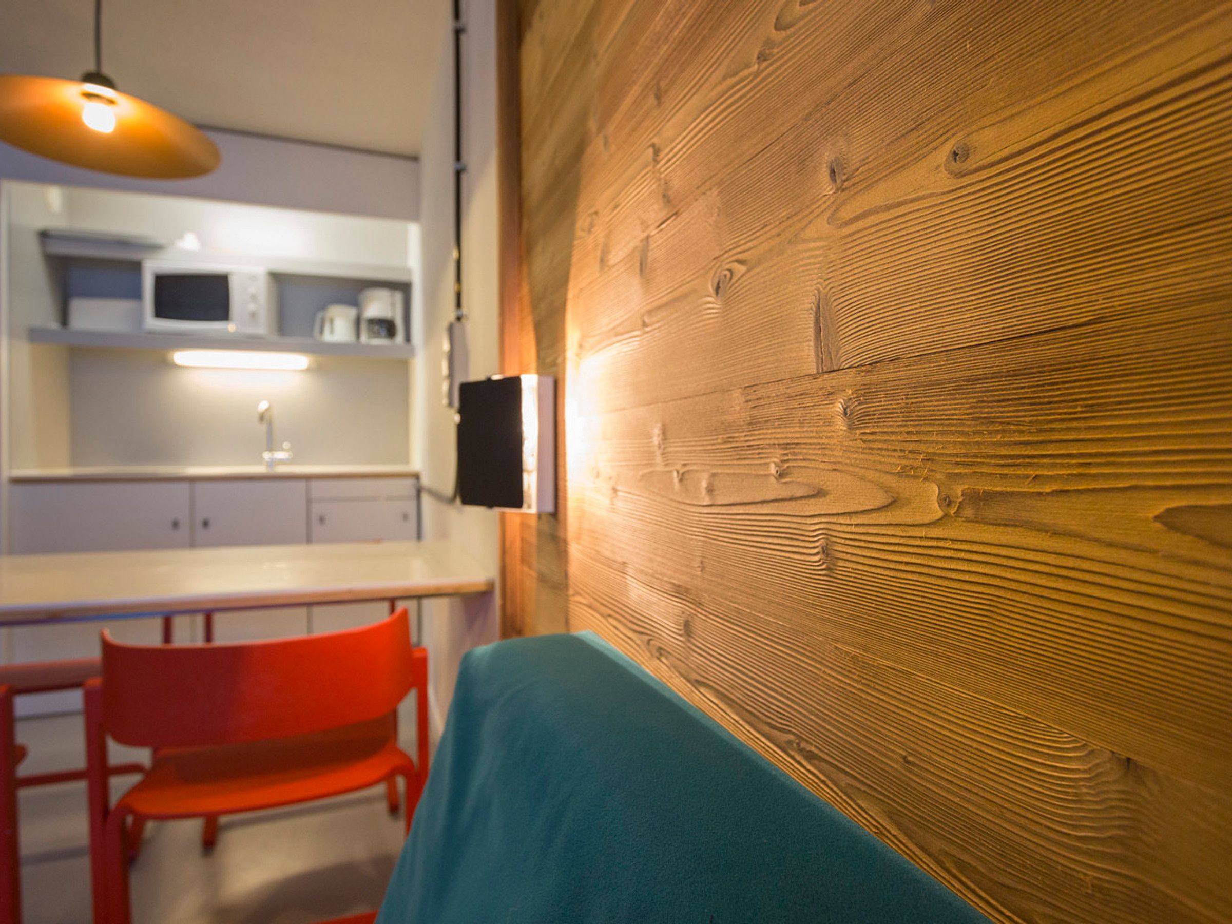 A modern kitchen with a wooden accent wall, a red chair, and a blue table.