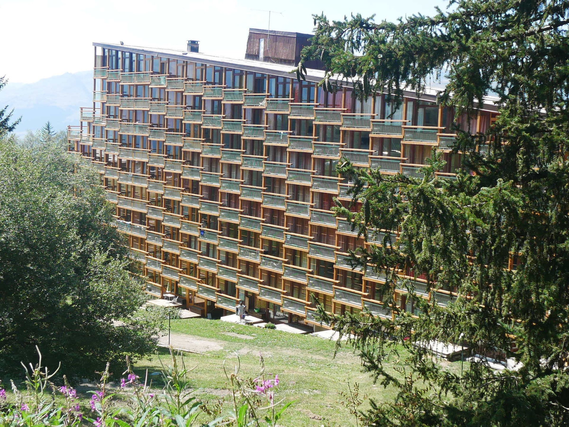 A multi-story hotel with a modern architectural design, featuring balconies and a view of the surrounding landscape.
