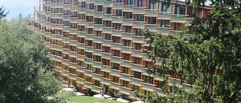 A multi-story hotel with a modern architectural design, featuring balconies and a view of the surrounding landscape.