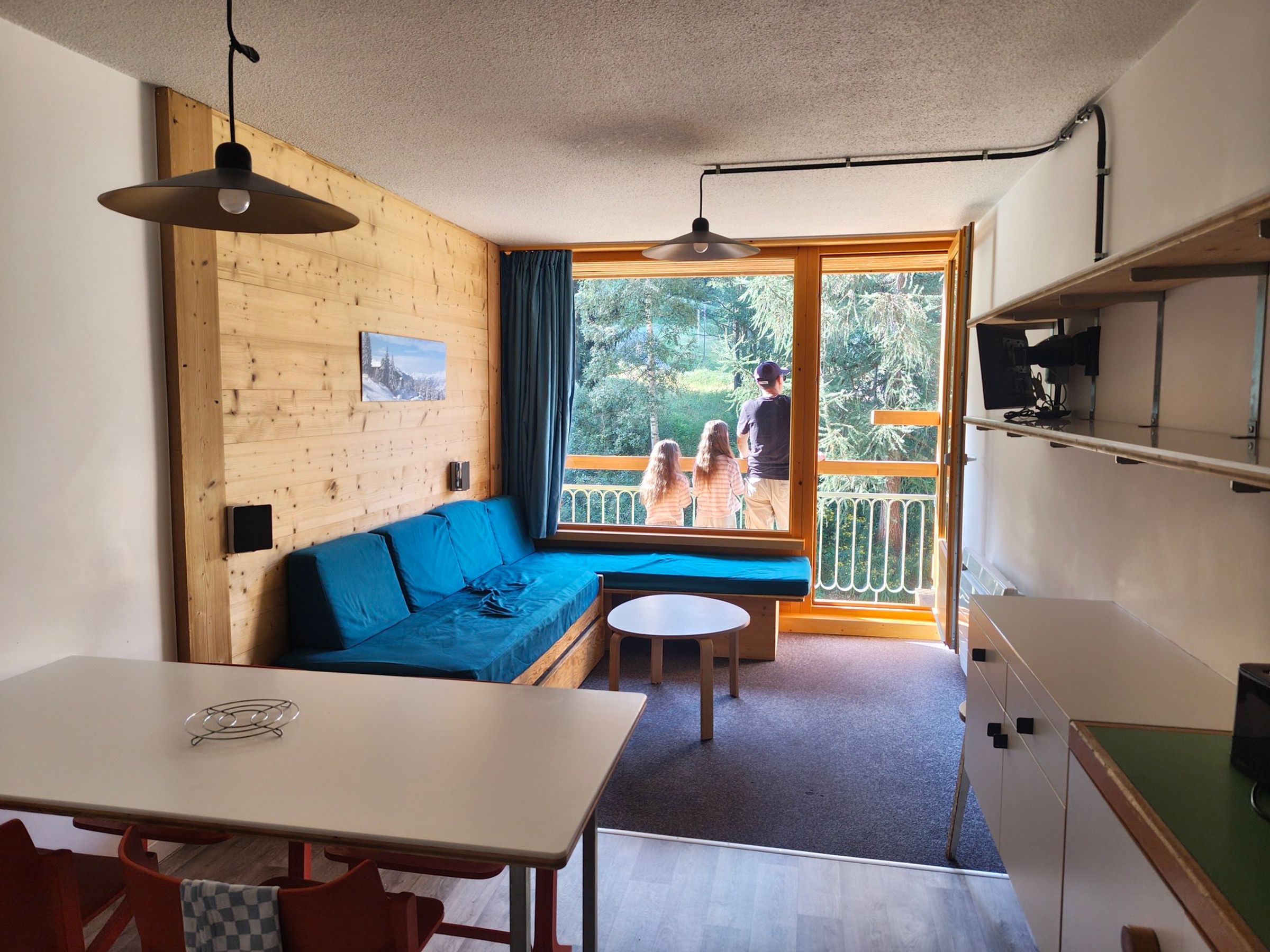Una habitación con una pared de madera, un sofá azul, una mesita y un balcón con barandilla.