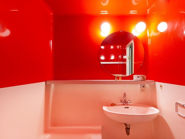 A bathroom with a white sink, a round mirror, and red walls.