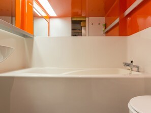 Ein Badezimmer mit einer weißen Badewanne, einer Toilette und einem Spiegel.