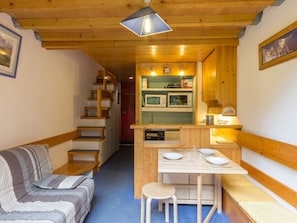 A compact room with a sofa, a small dining table with stools, a kitchenette with a microwave, and a staircase leading to another area.