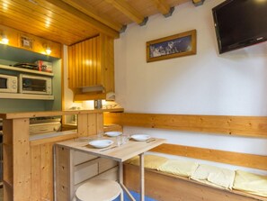 A wooden cabin interior with a dining table set for two, a bench, and a mounted television.