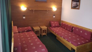 A cozy room with a wooden wall, two beds with floral bedding, a small table, and two wall-mounted lights. - Studio for 4, slopeside with balcony (Plagne Bellecôte)
