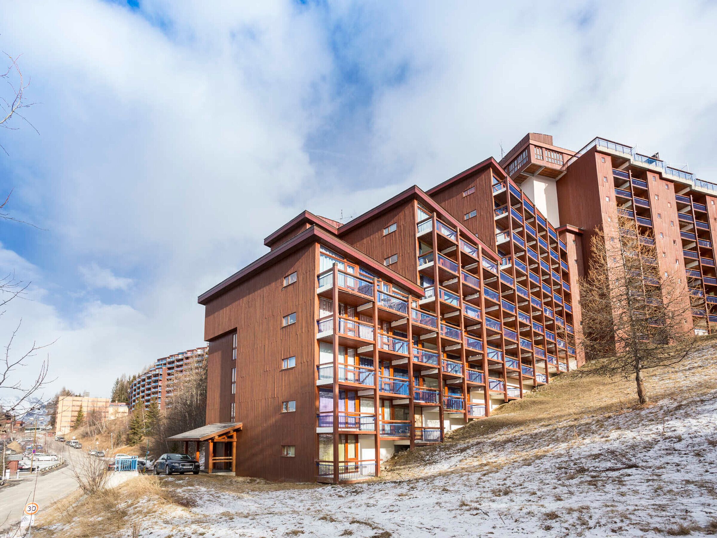 Ein mehrstöckiges Hotel mit Holzfassade, Balkonen und einer Skipiste im Hintergrund.