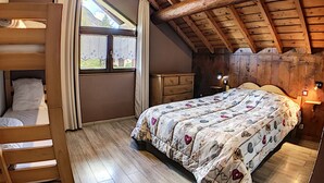 A cozy attic bedroom with a bunk bed, a large window with curtains, a wooden ceiling, and a bed with a floral bedspread. - Spacious and comfortable chalet with pool table, near lifts (Le Corbier)