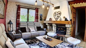 A cozy living room with a stone wall, a fireplace, a sofa, and a coffee table. - Spacious and comfortable chalet with pool table, near lifts (Le Corbier)