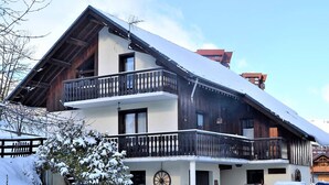 A two-story chalet with a balcony, a wooden exterior, and a snow-covered roof. - Spacious and comfortable chalet with pool table, near lifts (Le Corbier)