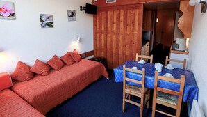 Una habitación acogedora con un sofá rojo, una mesita con mantel azul y paredes de madera.