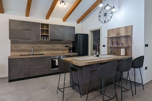 Una cuina moderna amb una illa central, tamborets de bar, forn de mur i nevera negra.