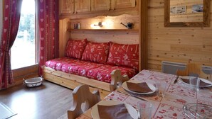 A cozy wooden cabin interior with a wooden bench, a dining table set with plates and glasses, and a small shelf with decorative items. - Cozy studio at the slopes - Pets allowed (Belle Plagne)