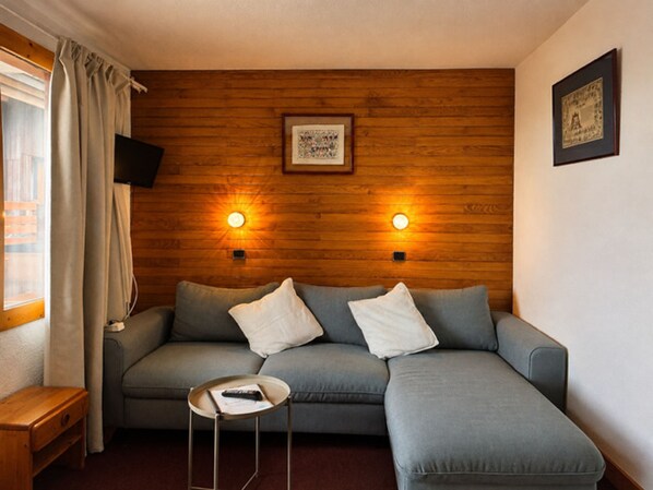 Una sala de estar moderna con un sofá seccional gris, una pequeña mesa auxiliar de madera y dos luces fijadas a la pared.