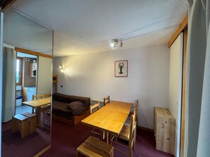 Una habitación compacta con una mesa de comedor de madera, un sofá y una kitchenette al fondo.