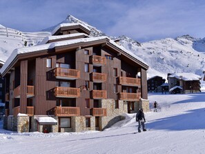 A multi-story wooden building with balconies, set against a snowy mountain backdrop. - Studio at slopes, balcony, 4 pers (Belle Plagne)