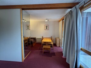 Una habitación con una mesa de madera, sillas, alfombra roja y una ventana con cortinas.