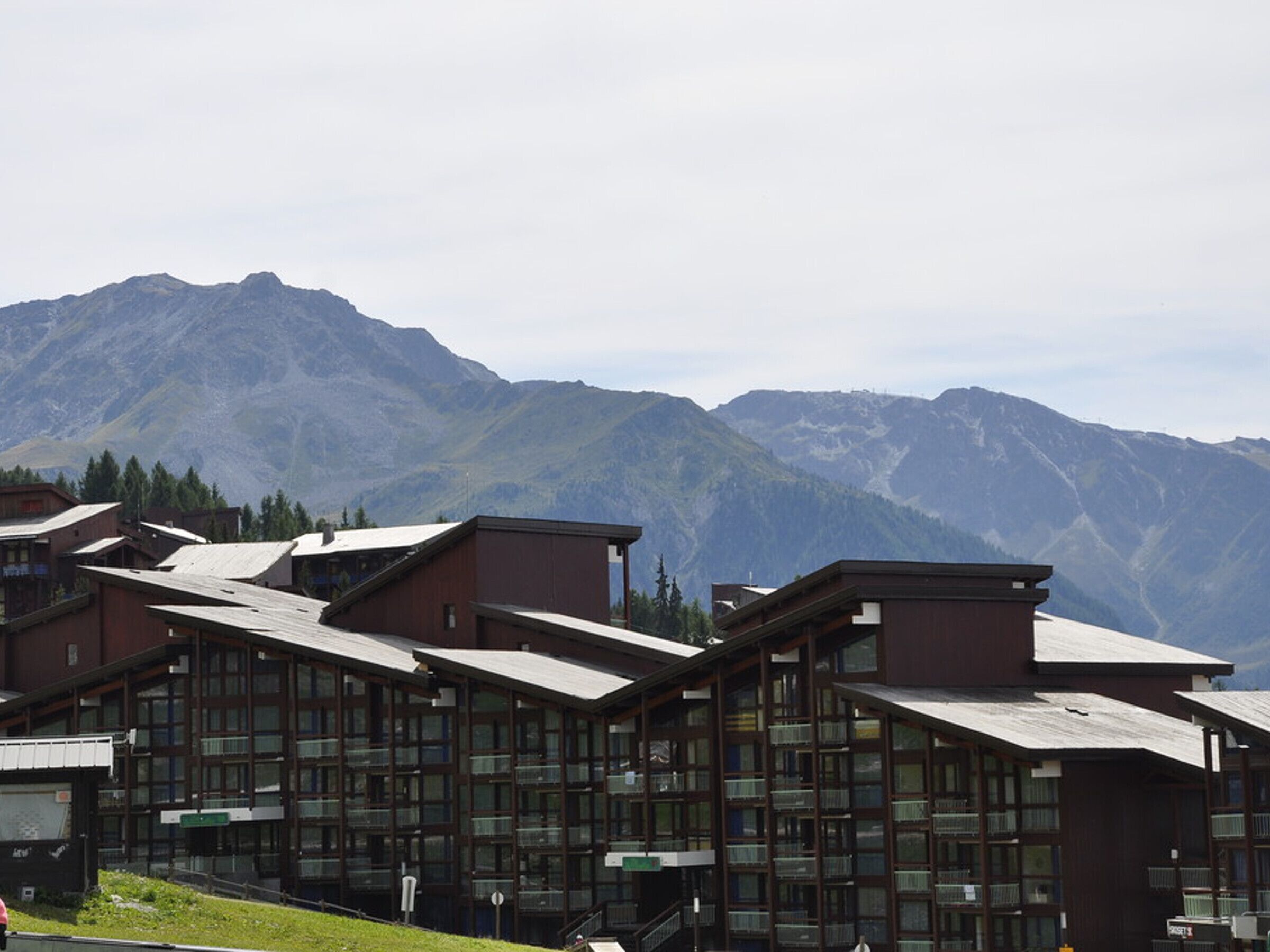 A modern building with large windows and a sloped roof, surrounded by mountains.