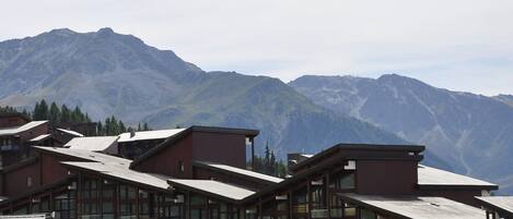 A modern building with large windows and a sloped roof, surrounded by mountains.
